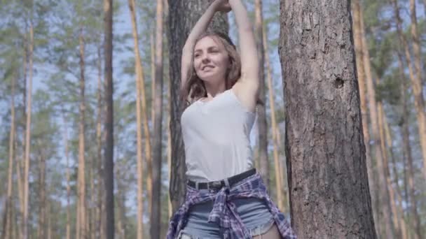 Mujer joven y bonita estirando su cuerpo, haciendo ejercicios en el bosque de pinos. Vida sana, unidad con la naturaleza, vida corta. Ocio exterior — Vídeos de Stock