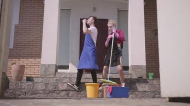 Kapı açılışı ve pozitif genç kadın ve erkek evin verandada dans. Çift birlikte ev temizliği. Mutlu rutin bir hayat. Ev işleri ve temizlik hizmeti konsepti.