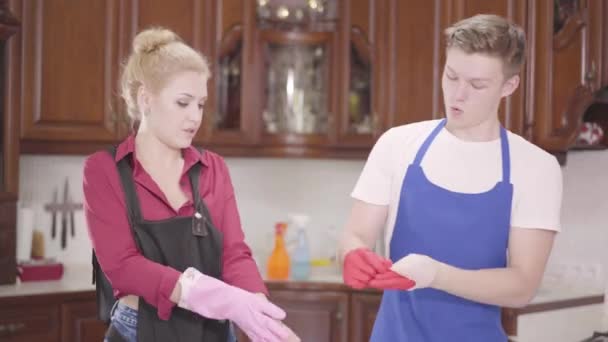 Schöne junge Frau und ein Mann in Schürzen, der Handschuhe und High Five auszieht. die Familie beendet die Hausreinigung gemeinsam. Hauswirtschaft Hausarbeit und Reinigungsservice-Konzept. — Stockvideo