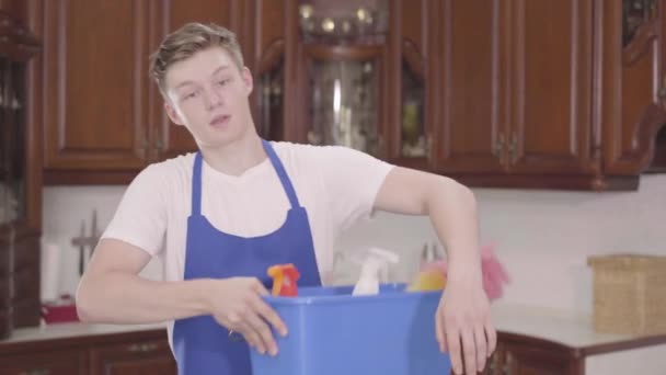 Retrato jovem bonito sorrindo homem tomando o cesto com detergentes e limpando a testa com a mão. Dia de limpeza. Serviço doméstico doméstico e conceito de serviço de limpeza — Vídeo de Stock