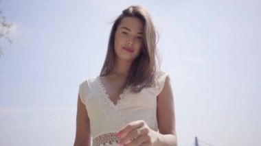 Uzun esmer saçlı portre güzel genç kız rıhtımda duran uzun beyaz yaz moda elbise giyiyor. Boş zaman güzel kadın açık havada saç doğrultma kamera bakıyor.