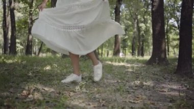 Tanınmayan genç kız parkta beyaz uzun yazlık elbise giymiş whirls. Dışarıda güzel bir kadının boş vakti. Yavaş çekim.