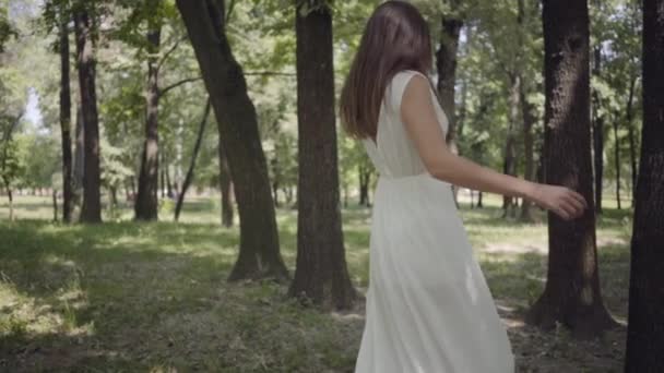 Αξιολάτρευτο νεαρό κορίτσι ντυμένος σε ένα λευκό μακρύ καλοκαιρινό φόρεμα περιστροφή στο πάρκο. Αναψυχή μιας ομορφης γυναίκας σε εξωτερικούς χώρους. Αργή κίνηση. — Αρχείο Βίντεο