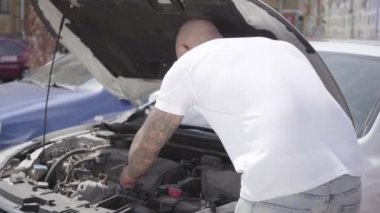 Araba kaputunun altına bakan kel orta doğulu adamın arka görünümü. Kırık arabayı dışarıda kontrol eden adam. Otomobil sabitleme.