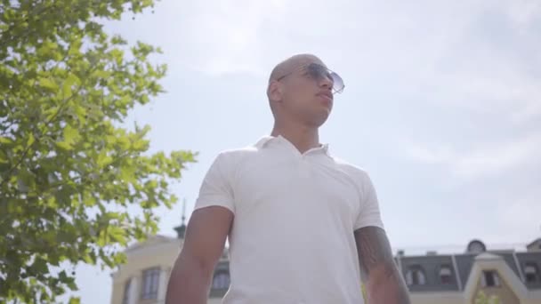 Hombre guapo calvo de Oriente Medio en gafas con un tatuaje de pie en la calle mirando a su alrededor . — Vídeos de Stock