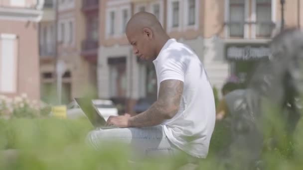 Hezký holohlavý Středovýchodní muž, který pracuje na ulici s laptopem sedícího na lavici. Koncept na volné noze. Obchodník pracující venku — Stock video