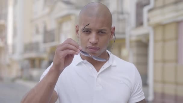 Portrait of handsome confident bald middle eastern man taking off glasses and looking in the camera standing on the street. Front view — Stock Video