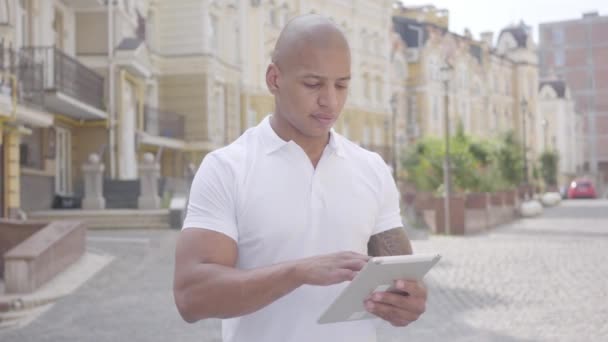 英俊自信的秃头中东男子在平板电脑上打字，站在老美丽的老建筑前的街道。专业技能，工作流程. — 图库视频影像