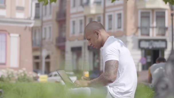 Handsome bald middle eastern man working with laptop sitting on the bench in the street. Freelance concept. The businessman working outdoors. Slow motion. — Stock Video