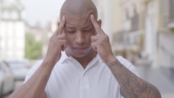 Portrait of handsome bald middle eastern man standing in the city street massaging his forehead with fingers. The guy is tired and stressed, he has headache. Intensive city lifestyle. Slow motion. — Stock Video