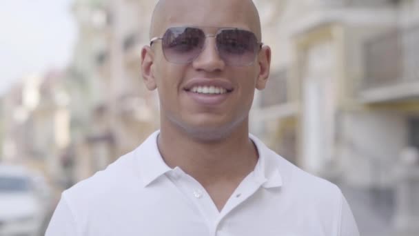 カメラを見てサングラスと白いTシャツを着て成功したハゲ中東の男のハンサムな自信の笑顔の肖像画。スローモーション. — ストック動画