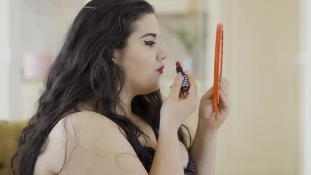 Portret van aantrekkelijke jonge plus size meisje doen make-up kijken in de spiegel. Zijaanzicht van mollige vrouw het schilderen van haar lippen met heldere rode lippenstift. Voorbereiden op de datum — Stockvideo
