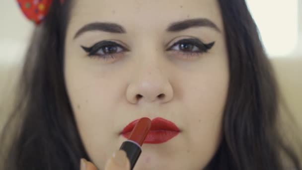 Primer plano retrato de linda chica con sobrepeso haciendo maquillaje mirando en la cámara. Mujer regordeta pintándose los labios con lápiz labial rojo brillante. Preparación de la fecha . — Vídeo de stock