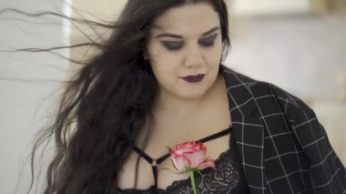 Gül tutan oldukça kilolu kızın yakın çekim portresi. Rüzgarda çırpınan saçlar. Kameraya bakan şehvetli bir tombul genç kadın. Şefkat, duygusallık. Yavaş çekim