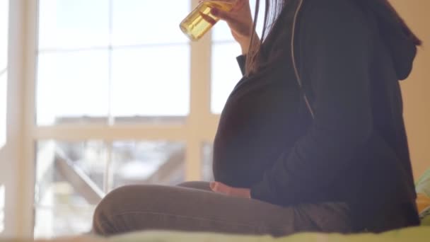 Giovane donna incinta irriconoscibile che beve birra da sola seduta sul divano di casa. Stile di vita malsano. Brutta abitudine. Il concetto di maternità malsana . — Video Stock