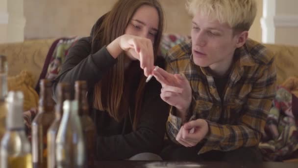 Porträtt av dålig söker drogmissbrukare man och kvinna röker en cigarett för två sitter på soffan hemma. Oroliga tonåringar. Missbruksproblem. — Stockvideo