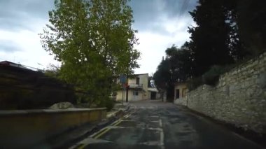 Yağmurdan sonra bulutlu bir günde evler, alabalıklar ve yol işaretleri ile dar bir sokakta hareket eden bir araba görünümü. Kıbrıs.