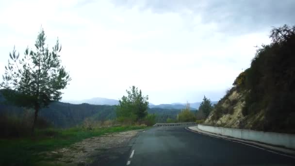 Vista desde un coche en movimiento en una calle estrecha con casas, truchas y señales de tráfico en un día nublado después de la lluvia. Chipre . — Vídeo de stock