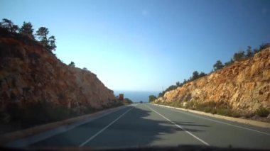 Yağmurdan sonra bulutlu bir günde evler, alabalıklar ve yol işaretleri ile dar bir sokakta hareket eden bir araba görünümü. Kıbrıs.