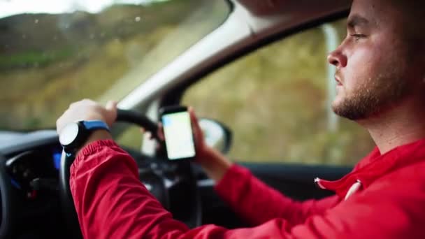 Porträt bärtigen jungen Mann am Steuer eines Autos mit einem Handy mit Navigationskarte. Zypern. Zeitlupe. — Stockvideo