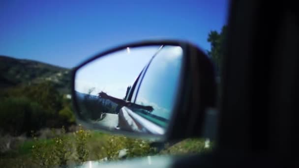 Reflectie van de hand niet-herkende passagier in de zijspiegel van een bewegende auto langs zonnige dagelijkse straat tijdens het reizen. Cyprus. Slow Motion. — Stockvideo