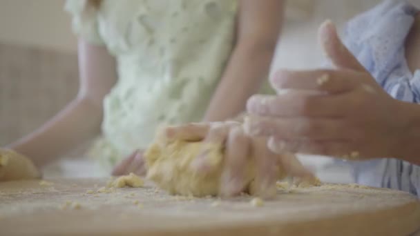 Маленькая дочь под присмотром матери выкатывает и формирует тесто для булочек. Закрыть — стоковое видео
