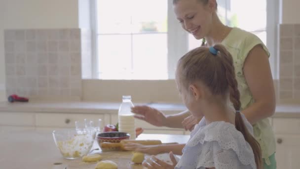 Widok z boku młodej kobiety i jej mała córka gotowanie ciasta w domu w kuchni. Dziewczyna wykańczania pracy i piątkę z matką. Mama i dziecko spędzają razem czas. Prawdziwa szczęśliwa Rodzina. — Wideo stockowe