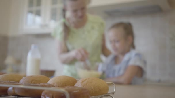 Des petits pains frais sur la table sur le fond de maman et petite fille s'amusent ensemble à faire des crêpes ou des gâteaux. Gros plan — Video