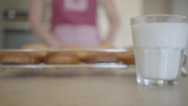 Два стакана молока на столе на заднем плане молодая женщина и свежеиспеченные булочки из духовки. Закрывай. Концепция рекламы — стоковое видео