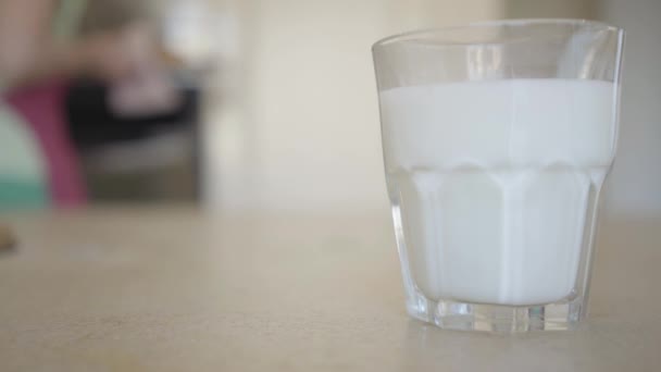 Närbild glas mjölk på bordet i bakgrunden en ung kvinna drar ut nybakade bullar från ugnen. Reklamkoncept — Stockvideo
