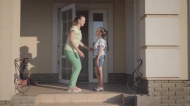 Portre genç sevimli anne büyük bir evin verandada duran onu sevimli kızı öpüşme. Çocuğa sarılan çocuk. Anne ve çocuk dışarıda birlikte vakit geçiriyorlar. Gerçek mutlu aile.