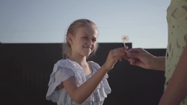 Belle fille gentille donnant à sa mère une fleur de pissenlit et lui souriant en soirée d'été au village 