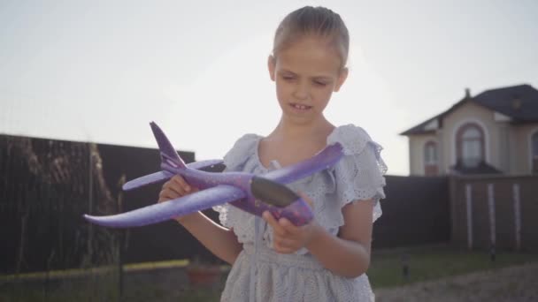 Retrato linda niña jugando con el pequeño avión de juguete de cerca. El niño pasa tiempo al aire libre en el patio trasero. Una infancia sin preocupaciones. Movimiento lento — Vídeos de Stock