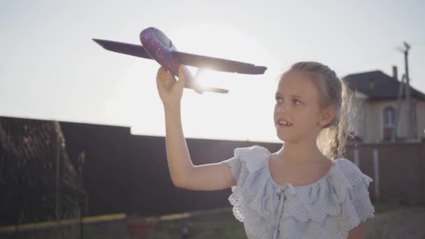 Портрет милая маленькая девочка держит маленький игрушечный самолет крупным планом. Ребенок проводит время на улице на заднем дворе. Беззаботное детство. Медленное движение — стоковое видео