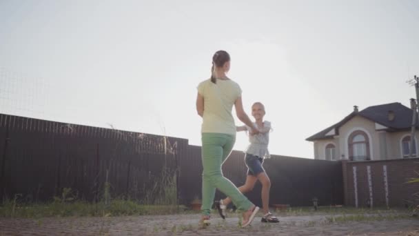 Happy little cute girl and her mother spinning around holding hands in the backyard. The woman and child having fun in front of shining sun. Mum and child spending time together outdoors. Slow motion — Stock Video