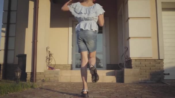 Hermosa niña en auriculares girando y bailando cerca de la casa en los rayos del sol de la noche. Chica disfrutando del tiempo libre al aire libre. Movimiento lento . — Vídeos de Stock