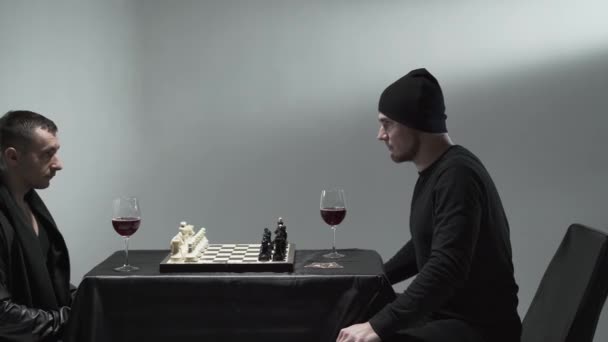 Kaksi shakkia pelaavaa miestä istuu pöydässä punaviinilasilliset edessään. Yksi tyyppi tekee siirtonsa. Studiokuva — kuvapankkivideo
