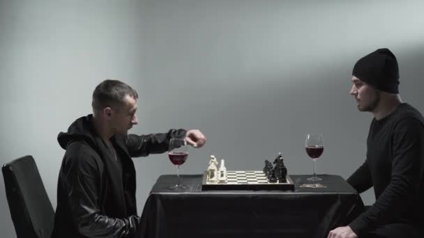 Deux hommes jouant aux échecs assis à la table avec les verres de vin rouge devant l'autre. Plan studio — Video