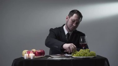 Zengin işadamı elma, üzüm ve bir kadeh kırmızı şarabın yanında bir parça et yiyor ya da tatıyor..