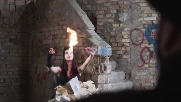 Молодая женщина с белым лицом, задувающая огонь в заброшенном здании перед стеной. Концепция шоу. Огненное шоу — стоковое видео