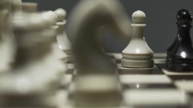 Beyaz ve siyah satranç taşları ile satranç tahtası yakın çekim. Gergin bir turnuva sırasında, rakip bir piyon alır.