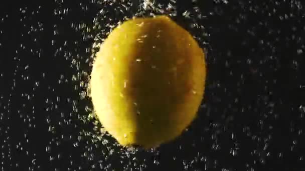 Verse citroen die op een zwarte achtergrond in het water valt. Citrus in water met bubbels. Biologisch voedsel, gezonde levensstijl, dieet. Video met accelerators. — Stockvideo