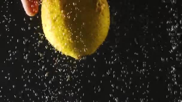 Mão humana segurando limão fresco sob a água no fundo preto. Citrus em água com bolhas. Alimentos orgânicos, estilo de vida saudável, dieta . — Vídeo de Stock