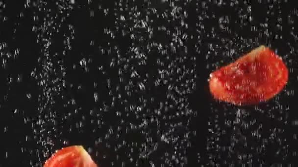 Tomaten schijfjes die in het watervallen op een zwarte achtergrond. Verse groente in het water met bubbels. Biologisch voedsel, gezonde levensstijl. Slow Motion. — Stockvideo