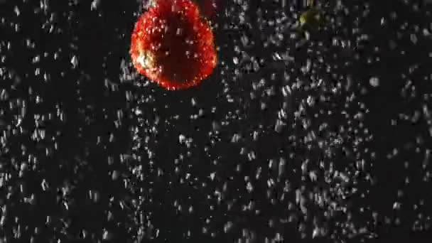Vallende verse aardbeien en kersen spatten in bruisend water op een zwarte achtergrond. Close-up. Video met versnelde. — Stockvideo