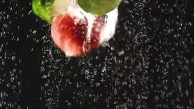 Salatalık ve domates dilimleri siyah arka plan üzerinde suya düşüyor. Kabarcıklar ile suda taze sebze. Organik gıda, sağlıklı yaşam tarzı, diyet. Yaz konsepti. Yavaş çekim ve hızlı hareket