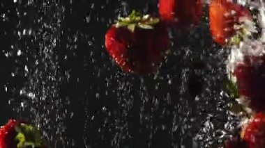 Düşen taze çilek ve kiraz siyah arka plan üzerinde köpüklü suya sıçrayan. Yakın çekim