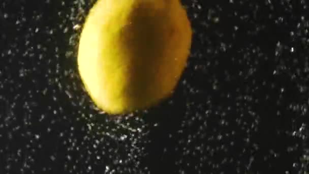 Citron frais tombant dans l'eau avec des bulles sur fond noir. Des baies fraîches dans l'eau. Baies biologiques, fruits, aliments sains. Mouvement lent . — Video