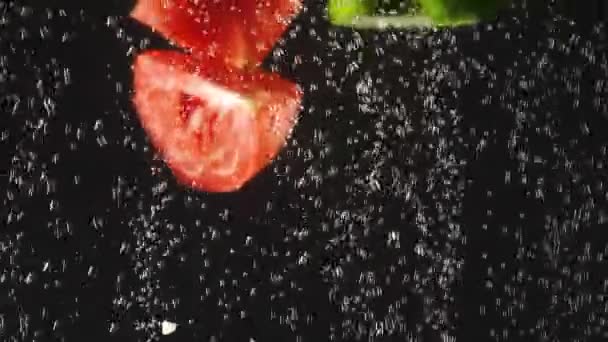 Komkommer en tomaten plakjes spetteren in het water op een zwarte achtergrond. Verse groente in het water met bubbels. Biologisch voedsel, gezonde levensstijl, dieet. Slow Motion — Stockvideo