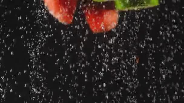 Fruits et légumes rouges et verts tombants éclaboussant dans de l'eau pétillante sur fond noir. Fusillade de macro. Gros plan — Video